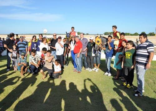 Proprietários, jóqueis e público na foto de premiação na pista