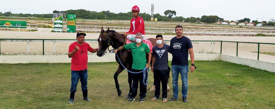 Proprietários e jóquei com o vencedor na foto de premiação, pista ao fundo