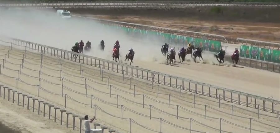 Páreo visto do alto da tribuna, com poeira na pista de areia